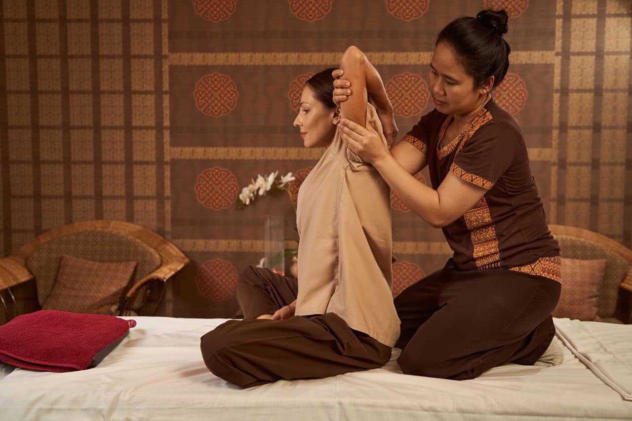 Thai massage practitioner guiding a seated arm stretch
